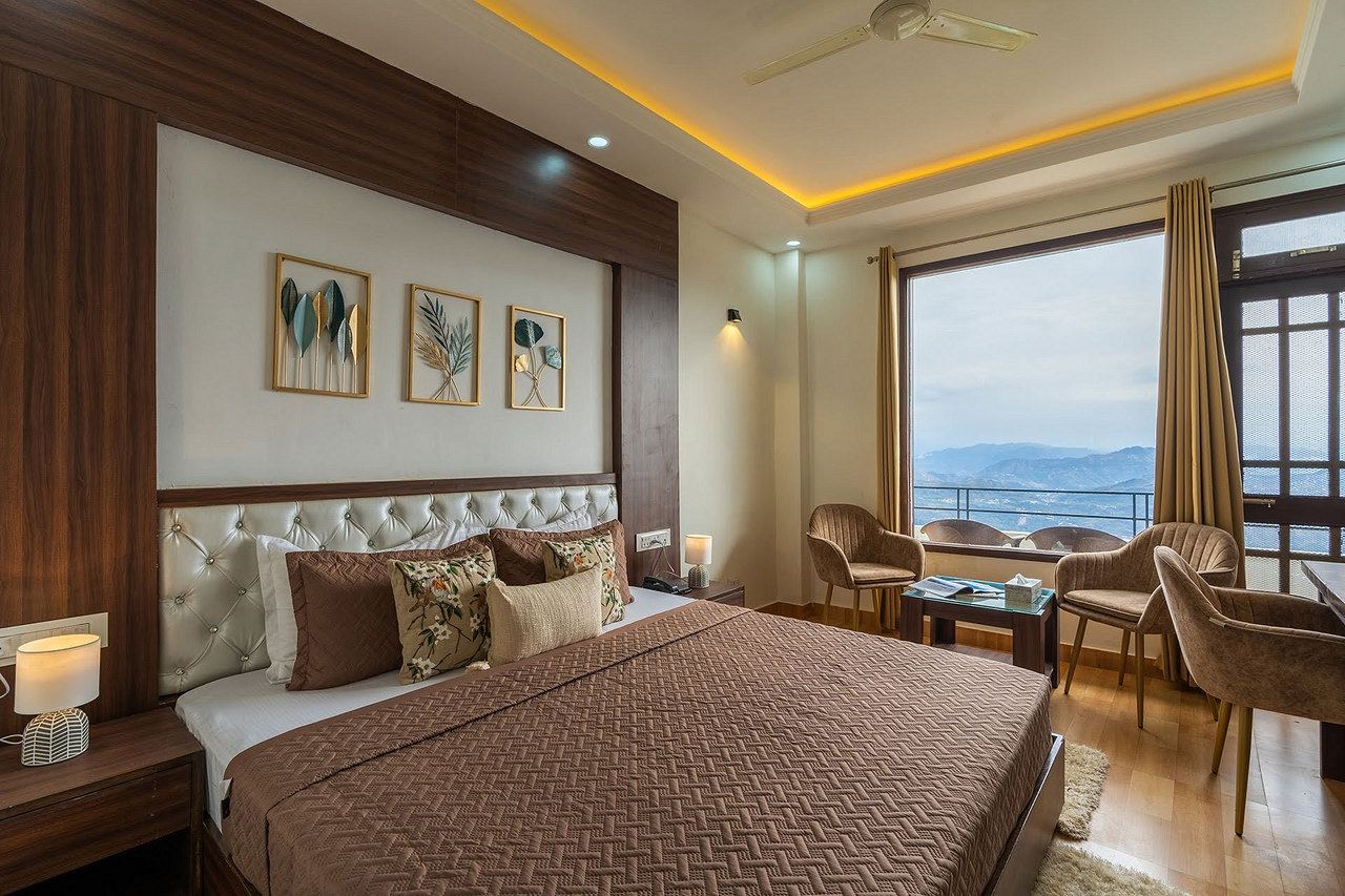 Deluxe Room: king bed with a brown cover, warm cove lighting and a large window onto the mountains