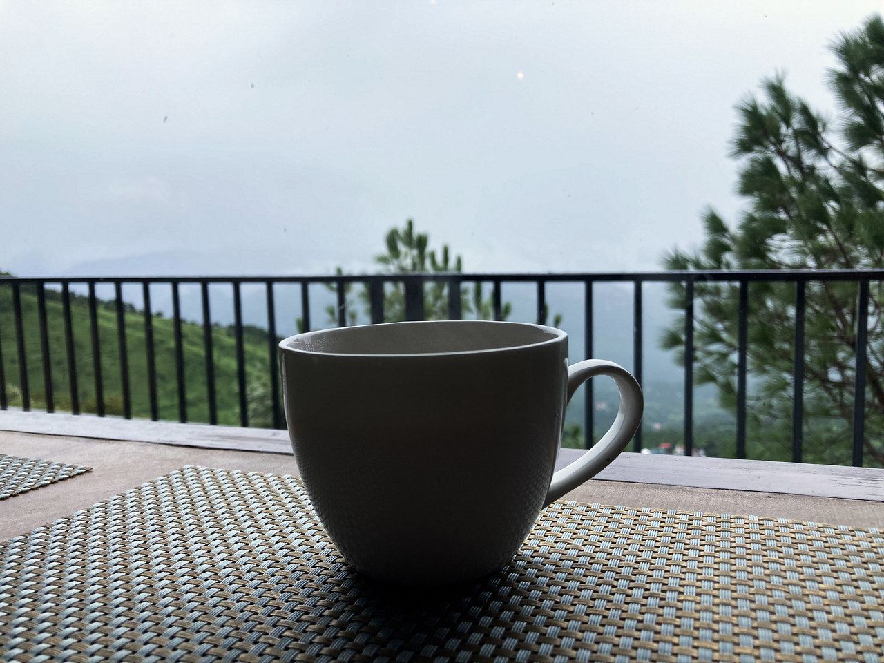 A cup of tea on a table at the balcony rail, with the hills behind