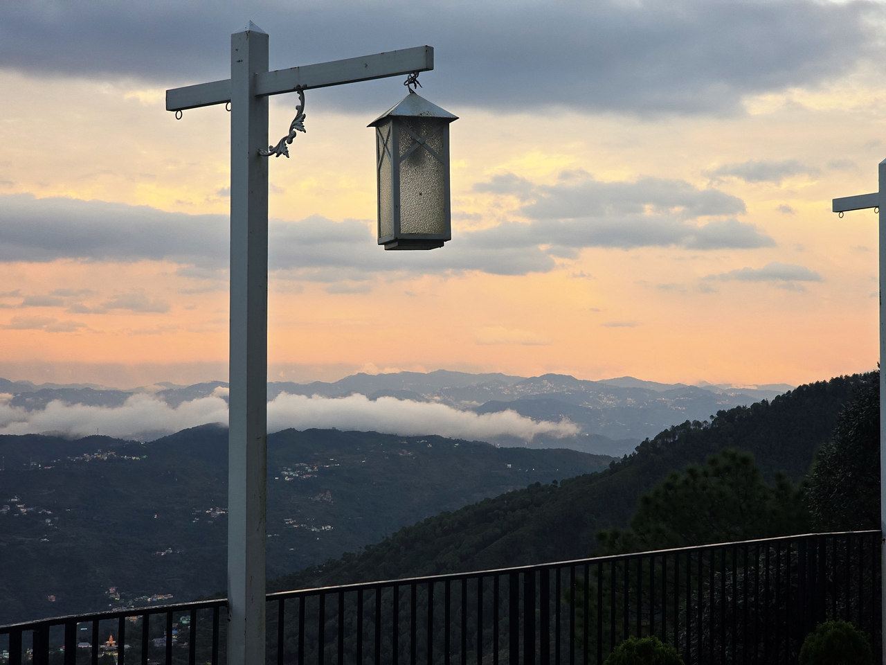 A lantern post on the terrace against a sunset sky and layered hills