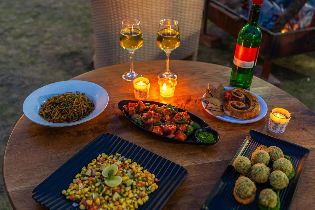 A dinner of grilled dishes on a round table on the lawn, with candles