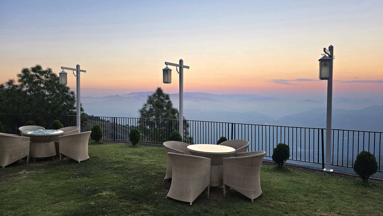 Cane chairs on the terrace at dusk, with a pink sky over the hills