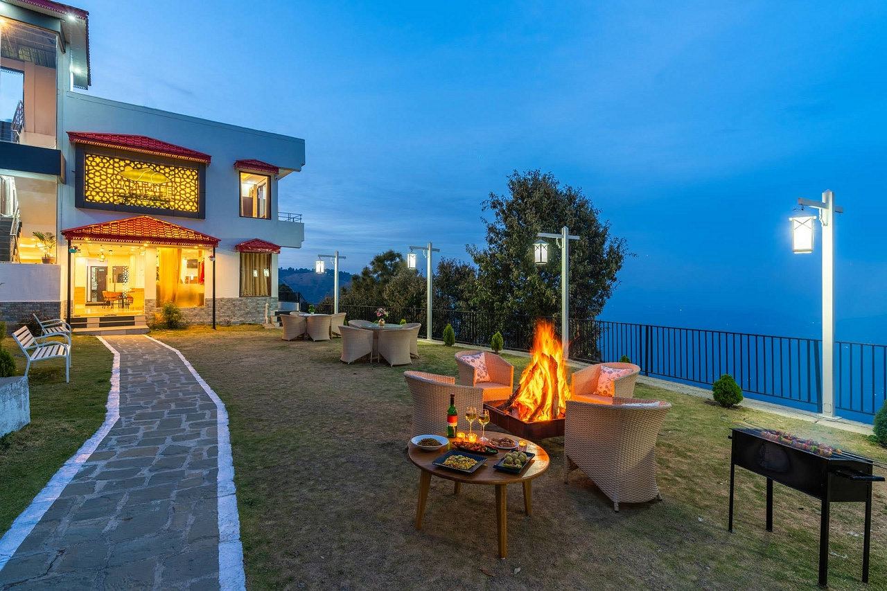 The lawn at dusk with a fire pit lit, the building glowing and the valley beyond