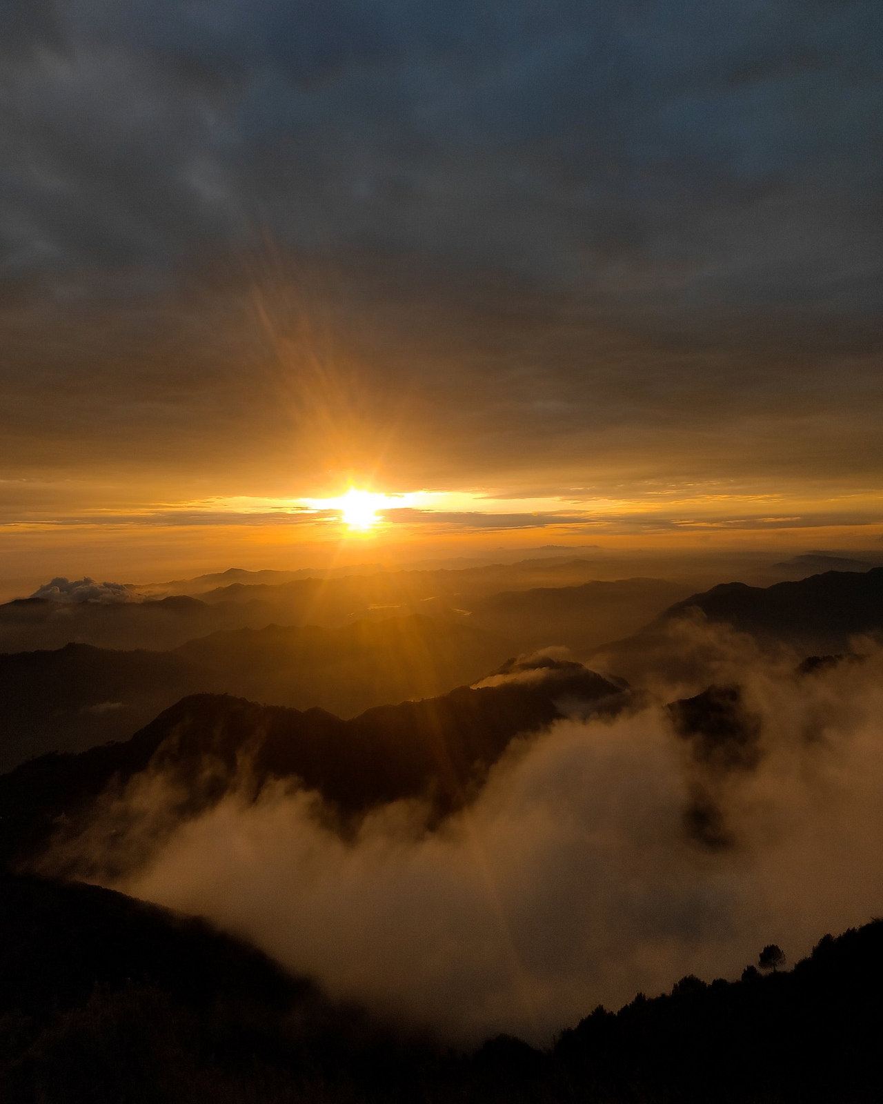 The sun low over layered ridges, with cloud filling the valleys below