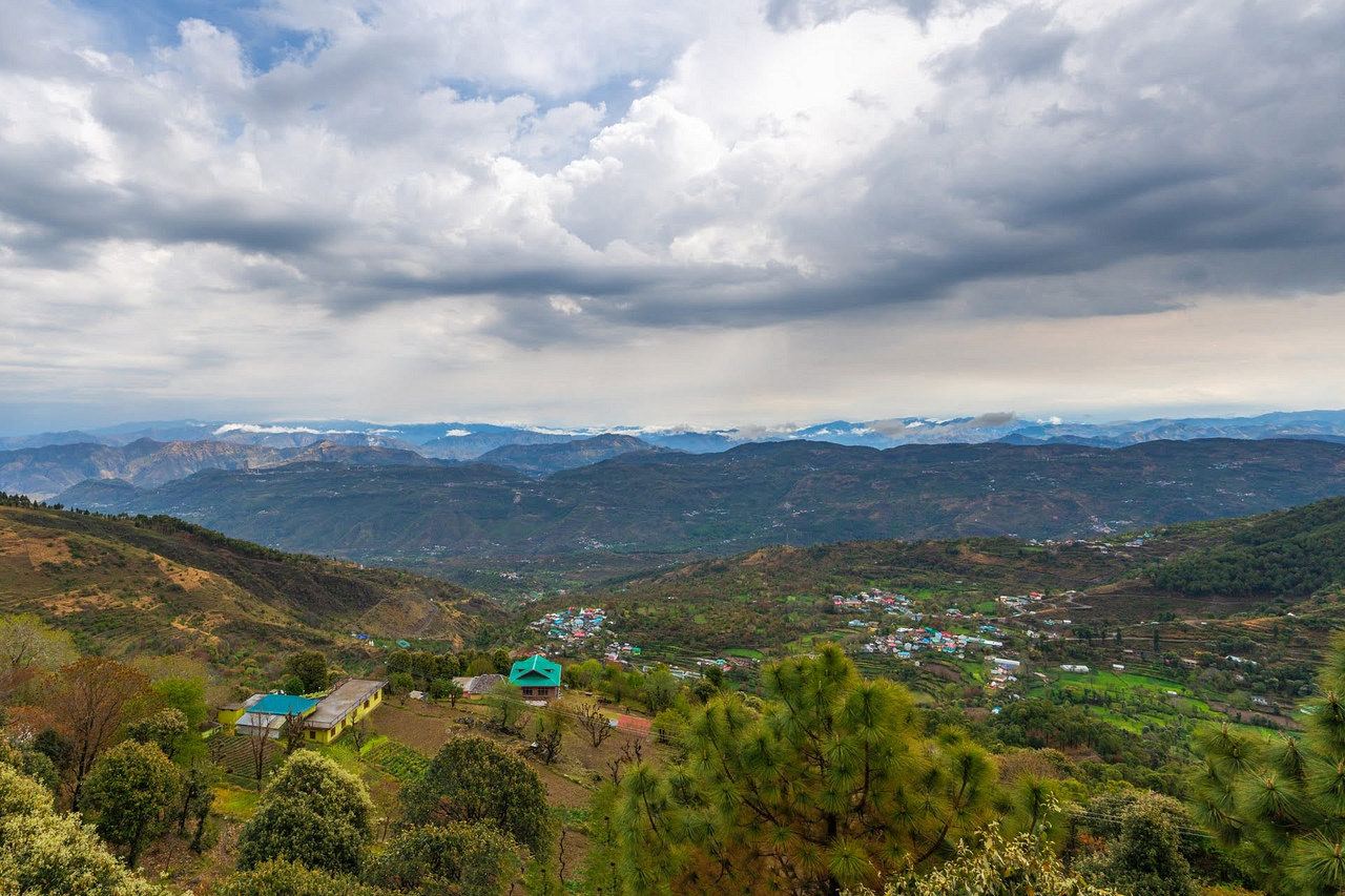 The green valley and the far ranges below the property, under a wide cloudy sky